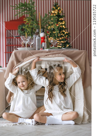 Little sisters hiding under the Christmas table. On the eve of the New Year and Christmas 119585722