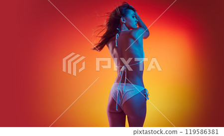 Rear view photo of woman in bikini stands, posing confidently in neon light against gradient studio background. Rear view photo of woman in bikini stands, posing confidently in neon light against gradient studio background. 119586381