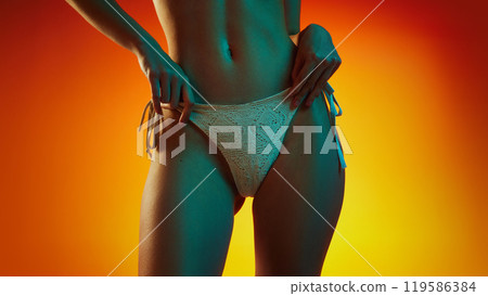 Close-up of lower back, highlighting curve of her waist and bikini bottom in neon light against gradient studio background. 119586384