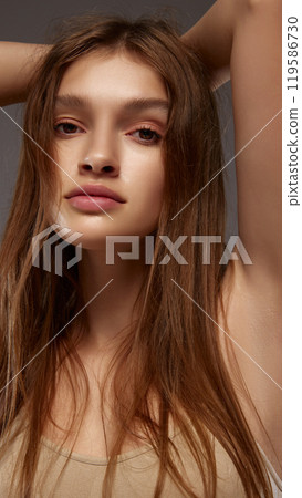 Close-up shot of model’s face with natural makeup, emphasizing fresh skin and natural beauty against warm grey background. Close-up shot of model’s face with natural makeup, emphasizing fresh skin and natural beauty against warm grey background. 119586730