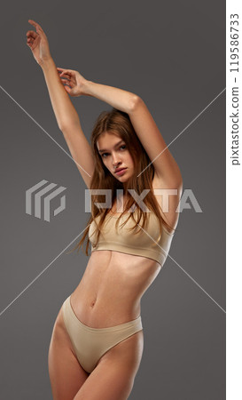 Young female model in posing,raising hands up, highlighting slim physique and natural beauty. against warm grey background. Young female model in posing,raising hands up, highlighting slim physique and natural beauty. against warm grey background. 119586733