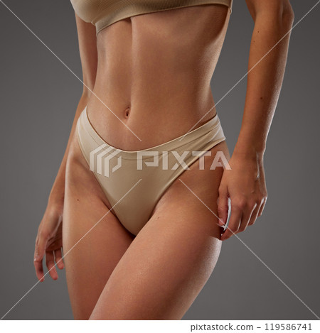 Close-up focusing on model's midsection. against warm grey background. Young woman dressed beige lingerie. 119586741