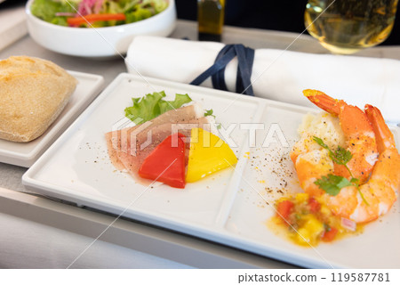 Delicious Business Class in-flight appetizer, salad, prosciutto and shrimp dish and champagne Delicious Business Class in-flight appetizer, salad, prosciutto and shrimp dish and champagne 119587781