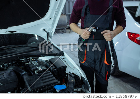Car service. An auto mechanic is standing near the car with a tool in his hands. Vehicle technical inspection 119587979