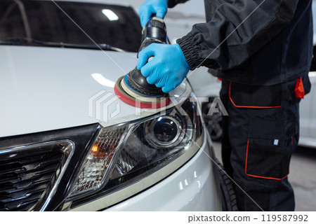 Serviceman polishing car body with machine in a workshop. 119587992