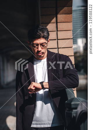 A man wearing glasses looking at his watch during a meeting A man wearing glasses looking at his watch during a meeting 119588122