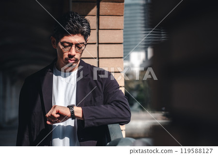 A man wearing glasses looking at his watch during a meeting A man wearing glasses looking at his watch during a meeting 119588127