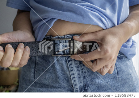 Hands unbuttoning leather belt on jeans 119588473