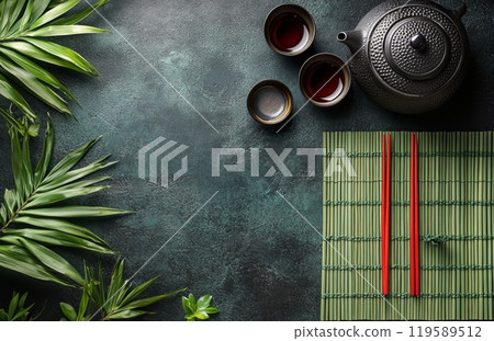 Traditional tea set displayed on a bamboo mat with green backdrop and decorative plants Traditional tea set displayed on a bamboo mat with green backdrop and decorative plants 119589512