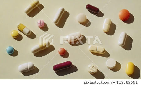 A variety of colorful pills and capsules arranged on a textured surface with crumbs scattered 119589561