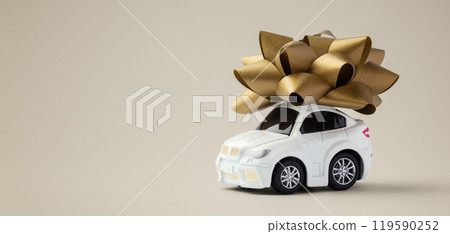 Car toy with gold bow on light gold background, car gift concept Car toy with gold bow on light gold background, car gift concept 119590252