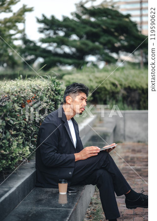 Man sitting outdoors working on a tablet Man sitting outdoors working on a tablet 119590622
