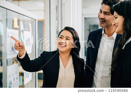 Diverse team of professionals comes together for a meeting, using a whiteboard to facilitate discussions on ideas, strategies, and plans. Demonstrating effective teamwork, leadership, and cooperation. 119590986