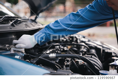 Auto mechanic writing on a clipboard checking car engine at workshop. Expertise in car service and repair technology-driven. Technician ensuring safety smiling at the challenge. 119590987