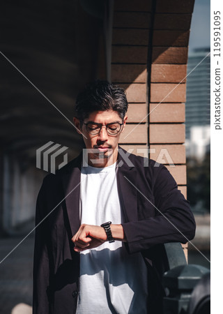 A man wearing glasses looking at his watch during a meeting A man wearing glasses looking at his watch during a meeting 119591095