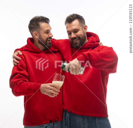 Portrait of two young brother dressed matching outfits posing together, when one brother pouring beer to glass in hands of another against white studio background. Collage. 119593115