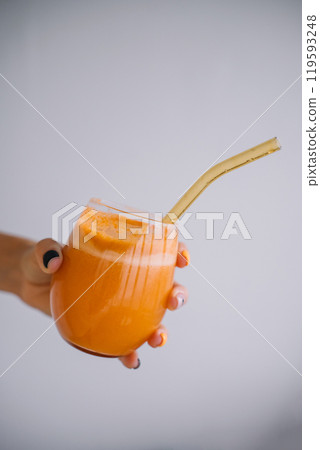 Refreshing orange smoothie served in a glass with a reusable straw on a plain background Refreshing orange smoothie served in a glass with a reusable straw on a plain background 119593248