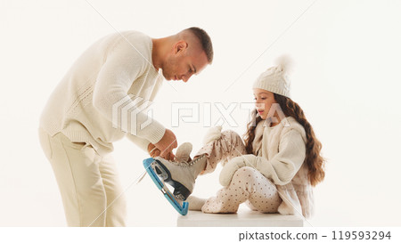 Dad adjusts his daughter's ice skates, making sure everything set for their day of fun on ice against white studio background. Dad adjusts his daughter's ice skates, making sure everything set for their day of fun on ice against white studio background. 119593294