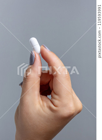 Female hand holding a white pill with fingers closeup against grey, Healthcare concept Female hand holding a white pill with fingers closeup against grey, Healthcare concept 119593991