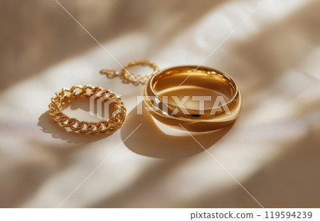 Elegant golden rings and chain displayed on a soft surface illuminated by warm sunlight 119594239