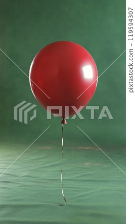 A single red balloon floats gracefully against a simple green backdrop in a quiet indoor setting 119594307