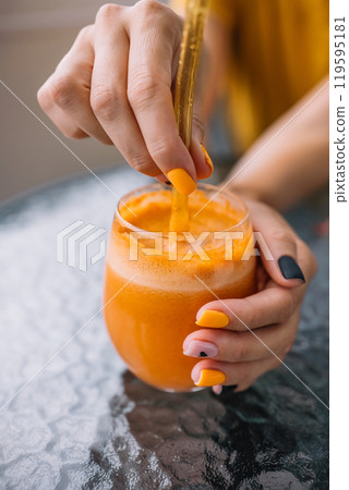 A person enjoys a refreshing orange drink with creative nails on a sunny day at a cafe A person enjoys a refreshing orange drink with creative nails on a sunny day at a cafe 119595181