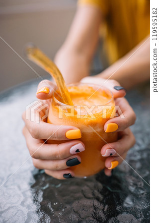 A person enjoys a refreshing orange drink with creative nails on a sunny day at a cafe 119595182