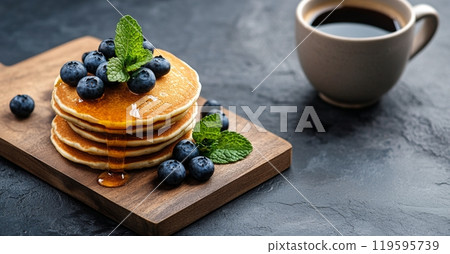 Delicious stack of fluffy pancakes topped with blueberries and mint beside a warm cup of coffee 119595739