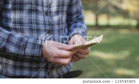 In a peaceful park, a person examines cash, emphasizing everyday life, finances, and leisure activities 119595905