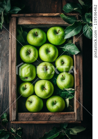 Fresh green apples arranged neatly in a rustic wooden crate with leaves on a dark background 119596462