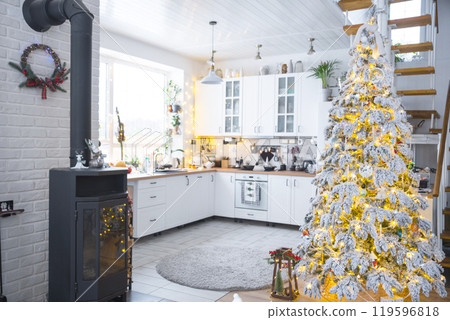 Festive white modern interior of house is decorated for Christmas and New Year in loft style with black stove, fireplace, Christmas tree. Potted plants, firewood in the woodpile 119596818