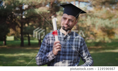 A proud graduate joyfully holding their diploma outdoors, celebrating their achievement with friends and family 119596987