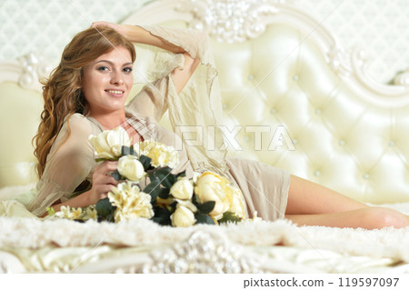 Beautiful young girl with a bouquet of flowers posing on the bed Beautiful young girl with a bouquet of flowers posing on the bed 119597097