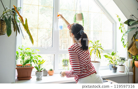 Woman manually washes the window of the house with rag cleaner and mop inside the interior with home plants on windowsill with attic. Restoring order and cleanliness in the spring, cleaning servise Woman manually washes the window of the house with rag cleaner and mop inside the interior with home plants on windowsill with attic. Restoring order and cleanliness in the spring, cleaning servise 119597316