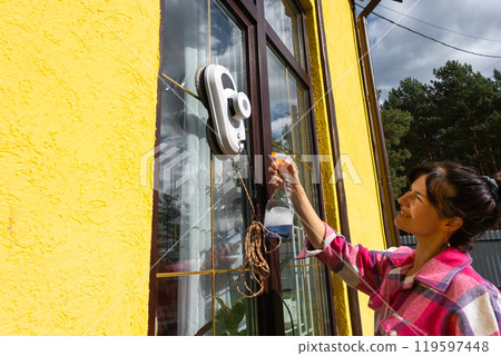 A woman launches a window cleaner robot of the house outside with a yellow facade. Household robotics, household assistant, cleaning servise A woman launches a window cleaner robot of the house outside with a yellow facade. Household robotics, household assistant, cleaning servise 119597448