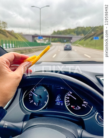 Eating French fries while driving on a highway with a clear view of dashboard. High quality photo 119598492