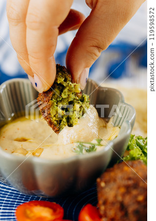 Dipping a crunchy falafel in creamy hummus for a delicious, plant based Mediterranean snack 119598572