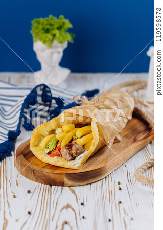 Juicy gyro wrap with fries, vegetables, and sauce, perfect for Mediterranean street food experience 119598578