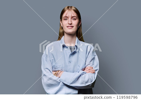 Beautiful young girl with crossed arms looking at camera on gray background 119598796