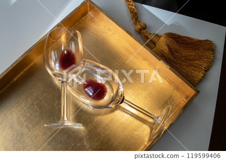 Used wine glasses, two half empty glasses of red wine on a golden tray background Used wine glasses, two half empty glasses of red wine on a golden tray background 119599406