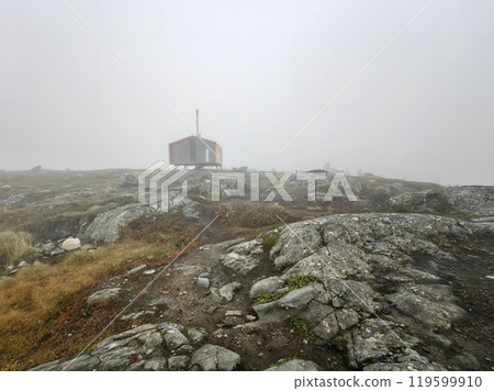 Fog-covered Volosyanaya Mountain in Kandalaksha with Dubldom shelter amid rocky terrain on a misty day 119599910