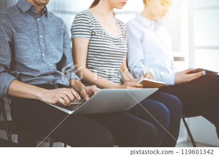 Group of casual dressed business people sitting in a line while waiting for a job interview in sunny office Group of casual dressed business people sitting in a line while waiting for a job interview in sunny office 119601342