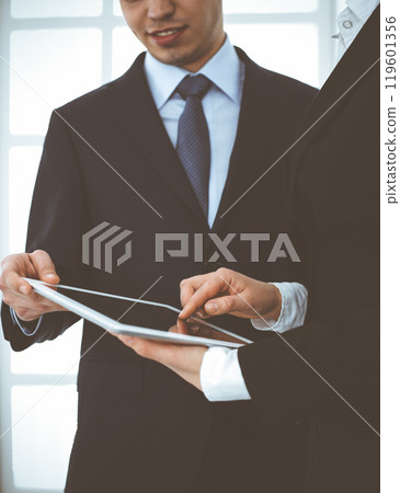 Businessman and woman using tablet computer for discussing questions in office. Partners or colleagues at meeting. Business cooperation concept Businessman and woman using tablet computer for discussing questions in office. Partners or colleagues at meeting. Business cooperation concept 119601356
