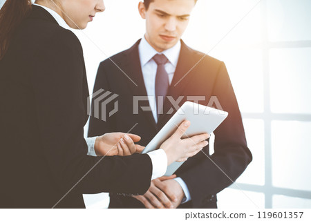Businessman and woman using tablet computer for discussing questions in sunny office. Partners or colleagues at meeting. Cooperation concept Businessman and woman using tablet computer for discussing questions in sunny office. Partners or colleagues at meeting. Cooperation concept 119601357