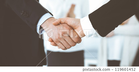 Businessman and woman shaking hands with colleagues at the background. Handshake at meeting in office. Concept of success in business Businessman and woman shaking hands with colleagues at the background. Handshake at meeting in office. Concept of success in business 119601452