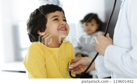 Woman-doctor examining a child patient by stethoscope. Cute arab boy at physician appointment. Medicine help concept 119601482