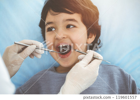 Cute arab boy sitting at dental chair with open mouth during oral checking up with doctor. Visiting sunny dentist office 119601557