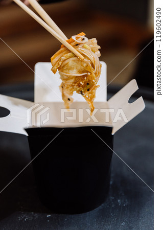 Chopsticks lifting fresh noodles from a takeaway box, showcasing a quick and delicious meal 119602490