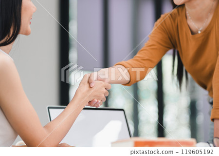 Smiling female executive makes a successful deal with a partner, shaking hands while standing at meeting table Smiling female executive makes a successful deal with a partner, shaking hands while standing at meeting table 119605192