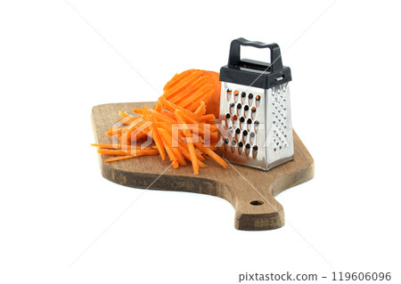 Grated carrots on a wooden cutting board with metal grater for healthy cooking and food preparation 119606096